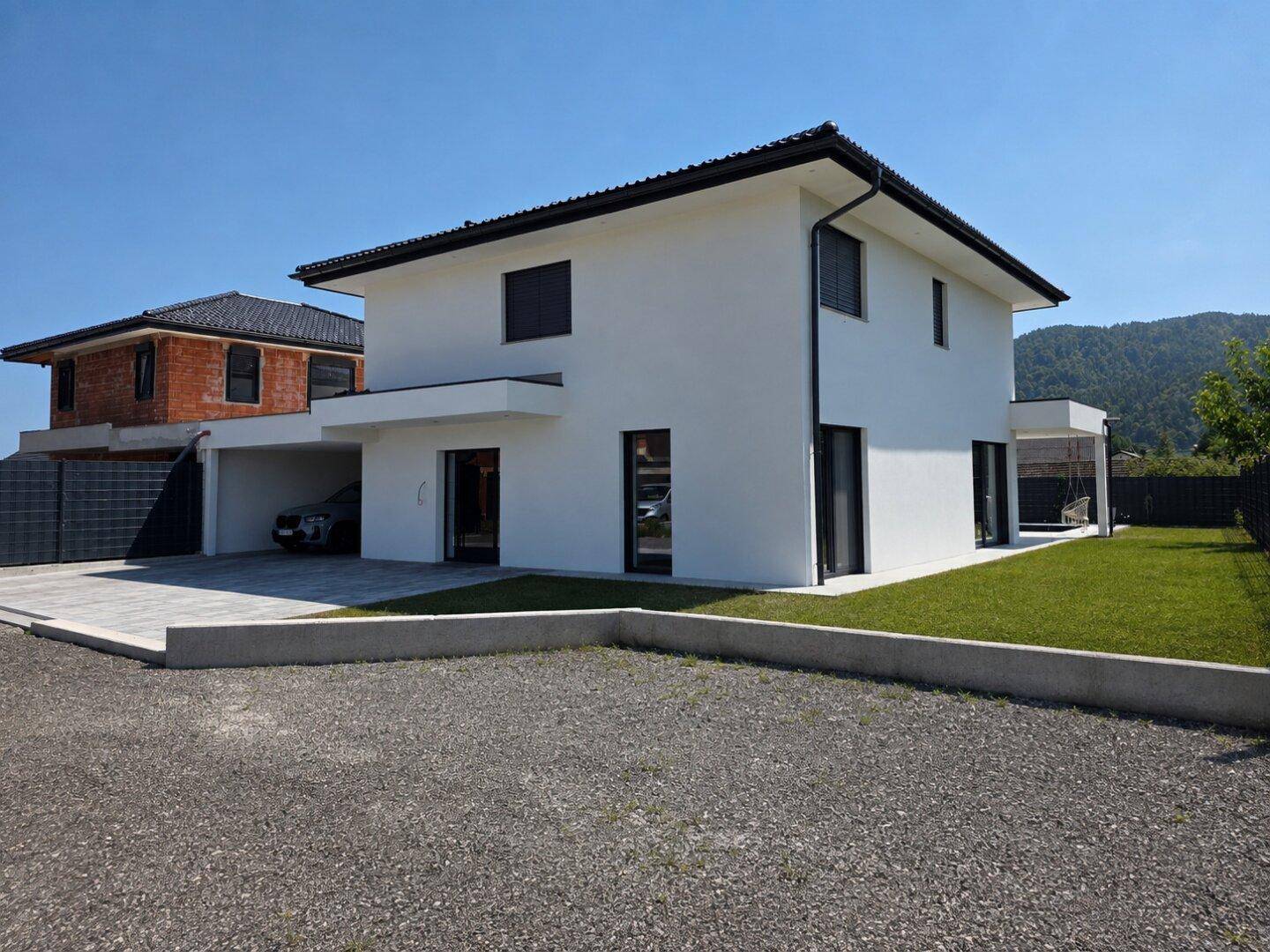 Modernes Einfamilienhaus mit weißer Fassade, Carport und gepflegter Außenanlage.