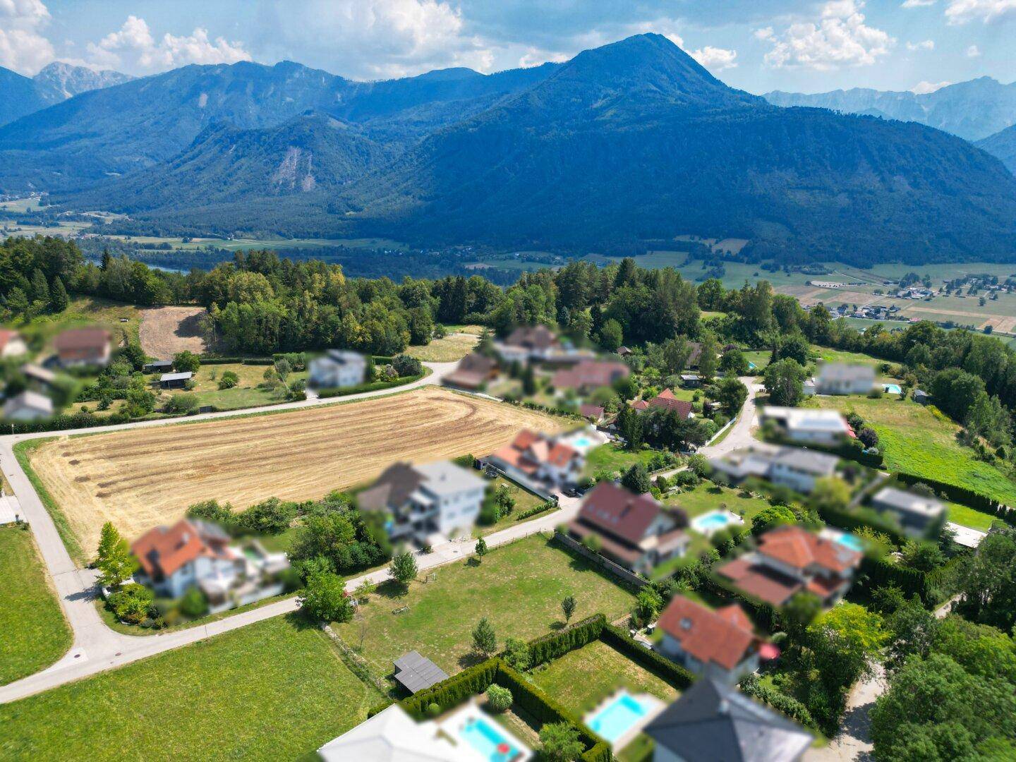 Weitläufige Luftaufnahme einer Wohngegend mit Häusern, Feldern und beeindruckendem Bergblick.