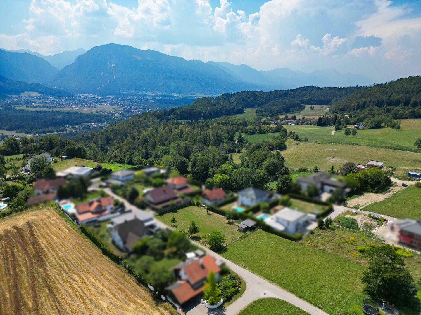 Luftaufnahme einer ländlichen Wohnsiedlung mit Häusern, Feldern und einer malerischen Bergkulisse.