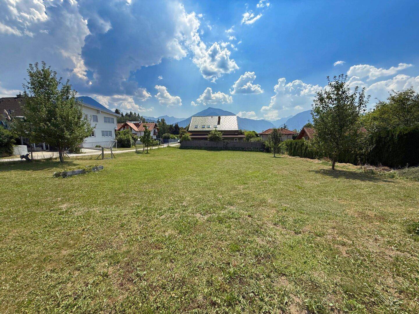 Geräumiges Gartengrundstück mit Rasen, umgeben von Häusern und einem weiten Bergblick.
