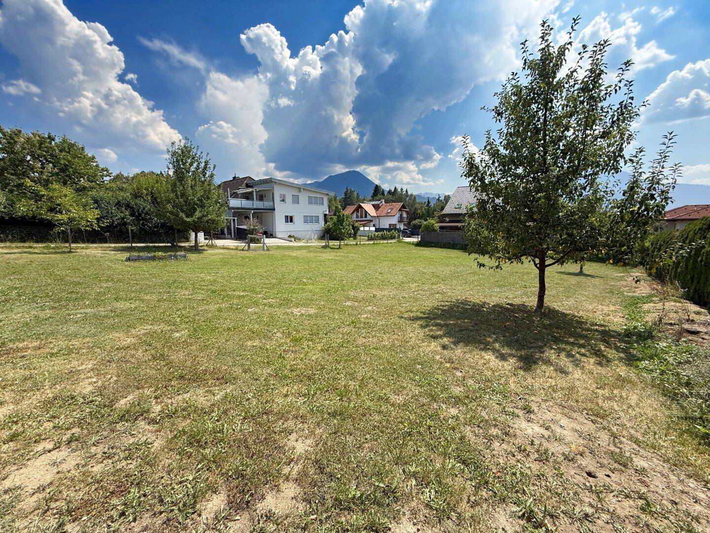 Weitläufiges Gartengrundstück mit Rasen, einem Baum und Häusern sowie Bergen in der Ferne.
