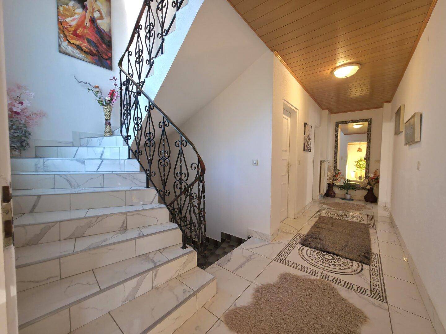 Heller Flur mit Marmorfliesen, einer eleganten Treppe und einem großen Spiegel.