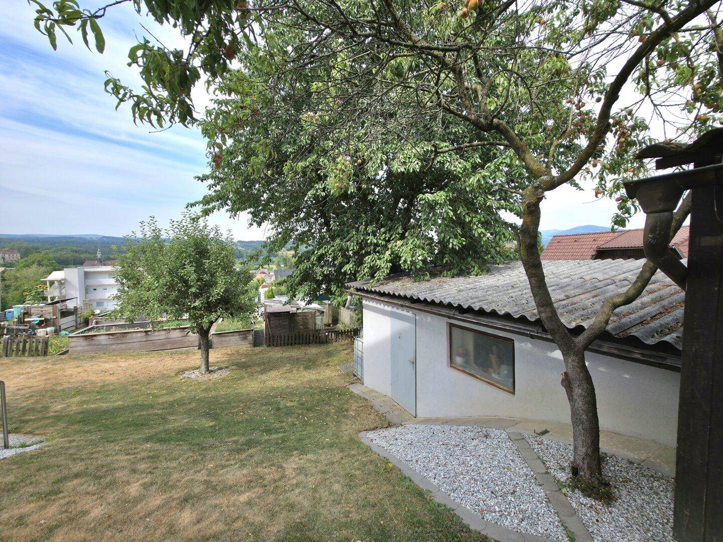Gartenbereich mit Schuppen, Bäumen und weitem Blick über die hügelige Landschaft.
