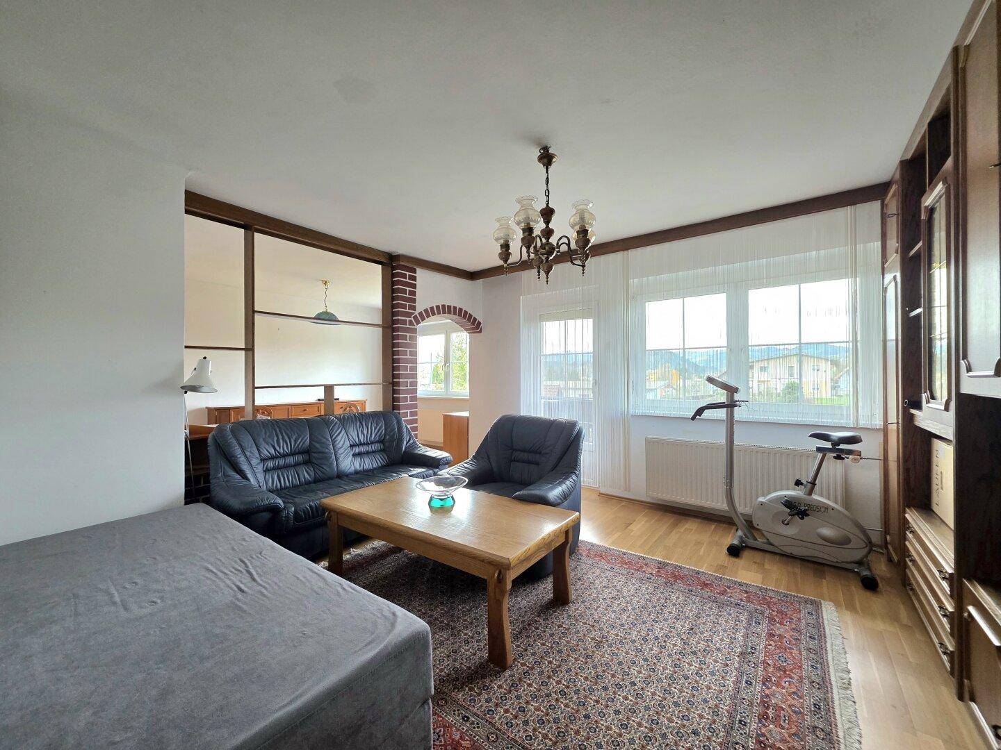 Helles Wohnzimmer mit Parkettboden, Ledersofa und Ausblick ins Grüne durch große Fenster.