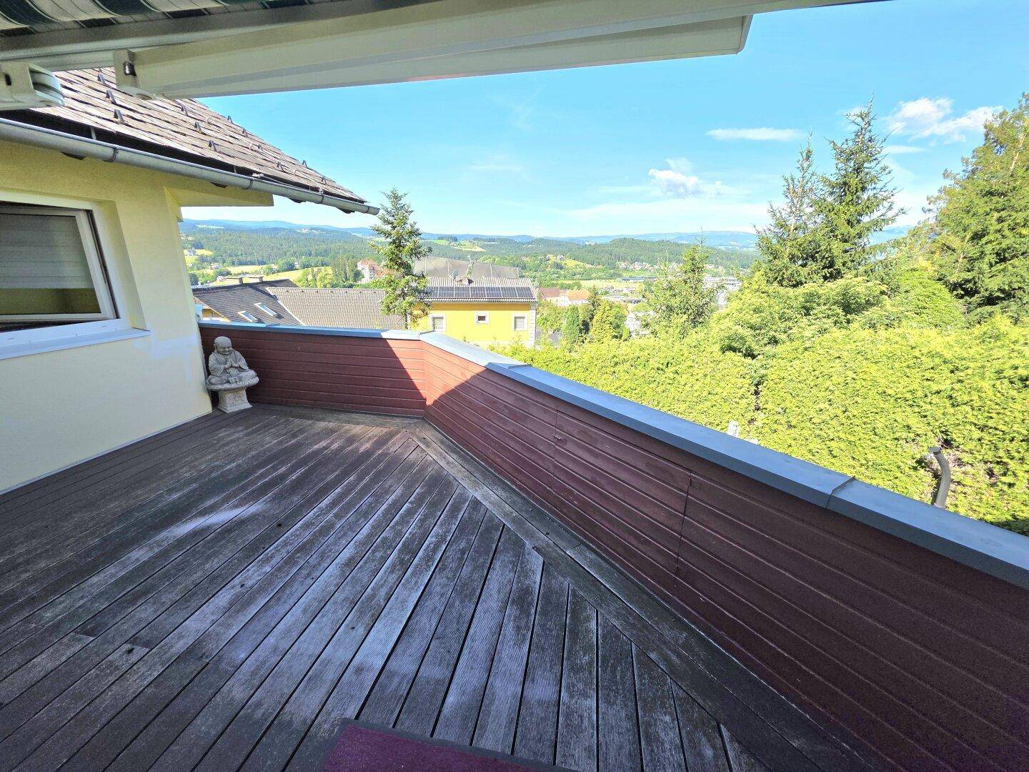 Geräumiger Holzbalkon mit schöner Aussicht auf die umliegende Landschaft und grüne Hügel.