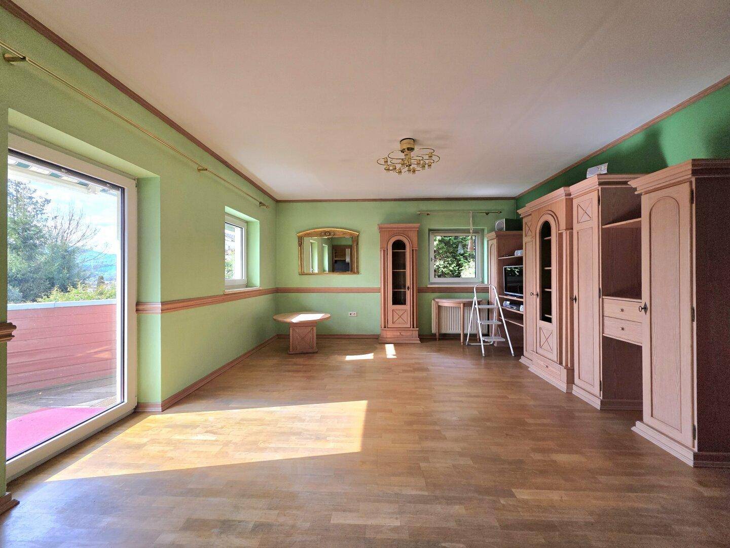 Großes Wohnzimmer mit Parkettboden, grünen Wänden und Einbauschränken, hell durch Tageslicht.