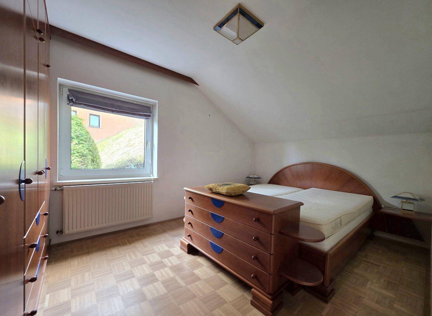 Gemütliches Schlafzimmer im Dachgeschoss mit Holzboden, Dachschräge und einem Fenster.
