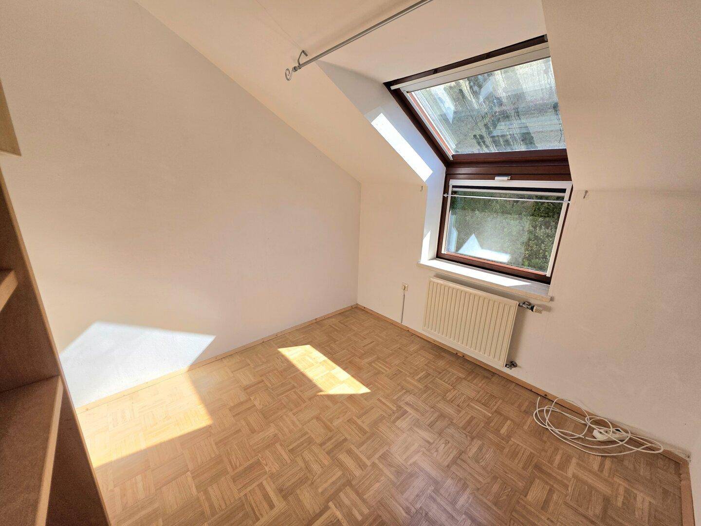 Helles Zimmer im Dachgeschoss mit Parkettboden, Dachfenster und Dachschräge, gut belichtet.