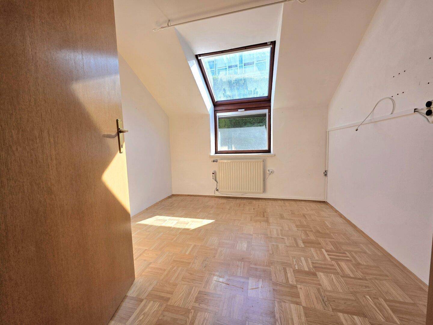 Lichtdurchflutetes Zimmer im Dachgeschoss mit Parkettboden, Dachfenster und Dachschräge.