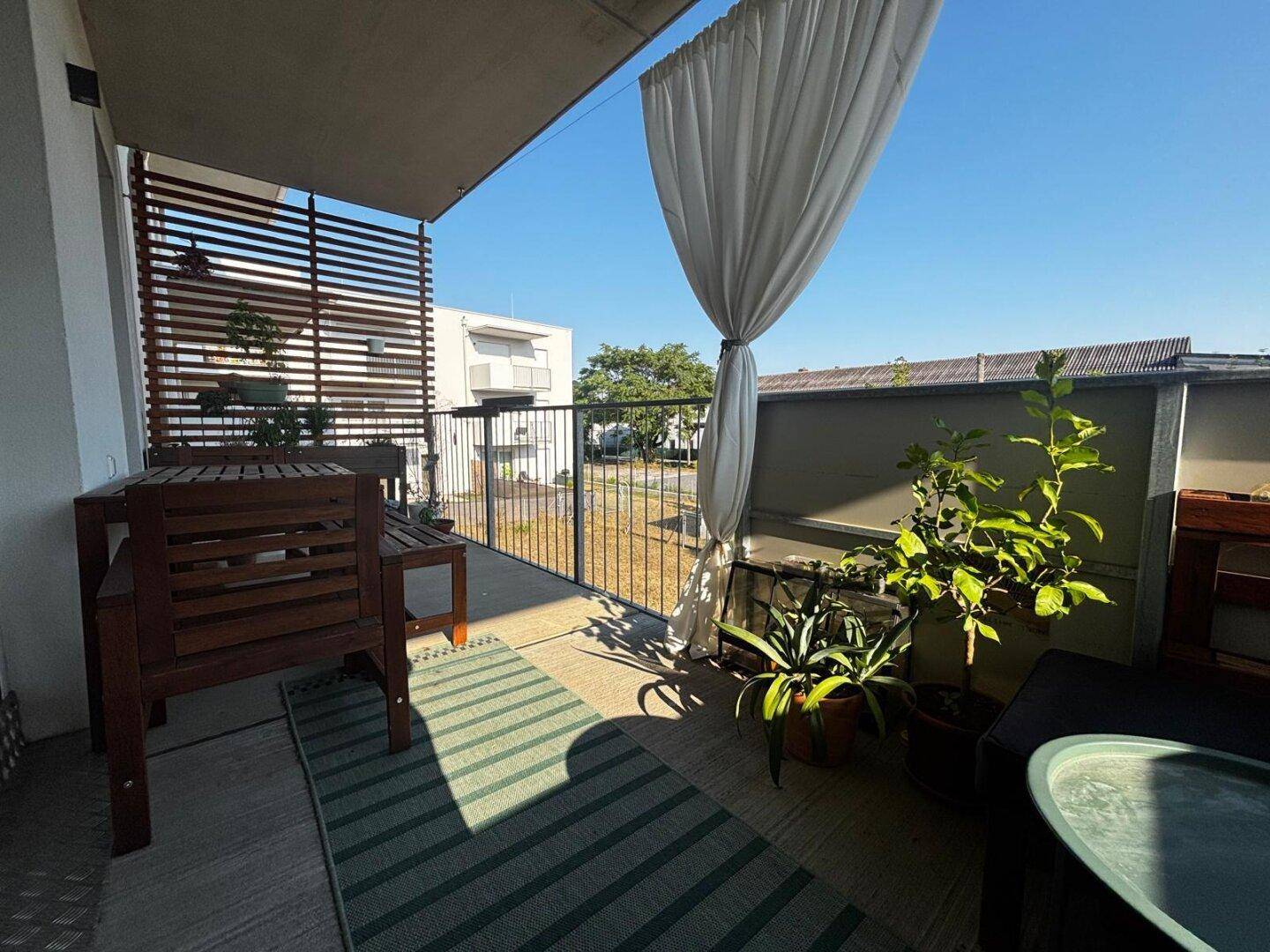 Gemütlicher Balkon mit Holztisch, Pflanzen und Blick ins Grüne.