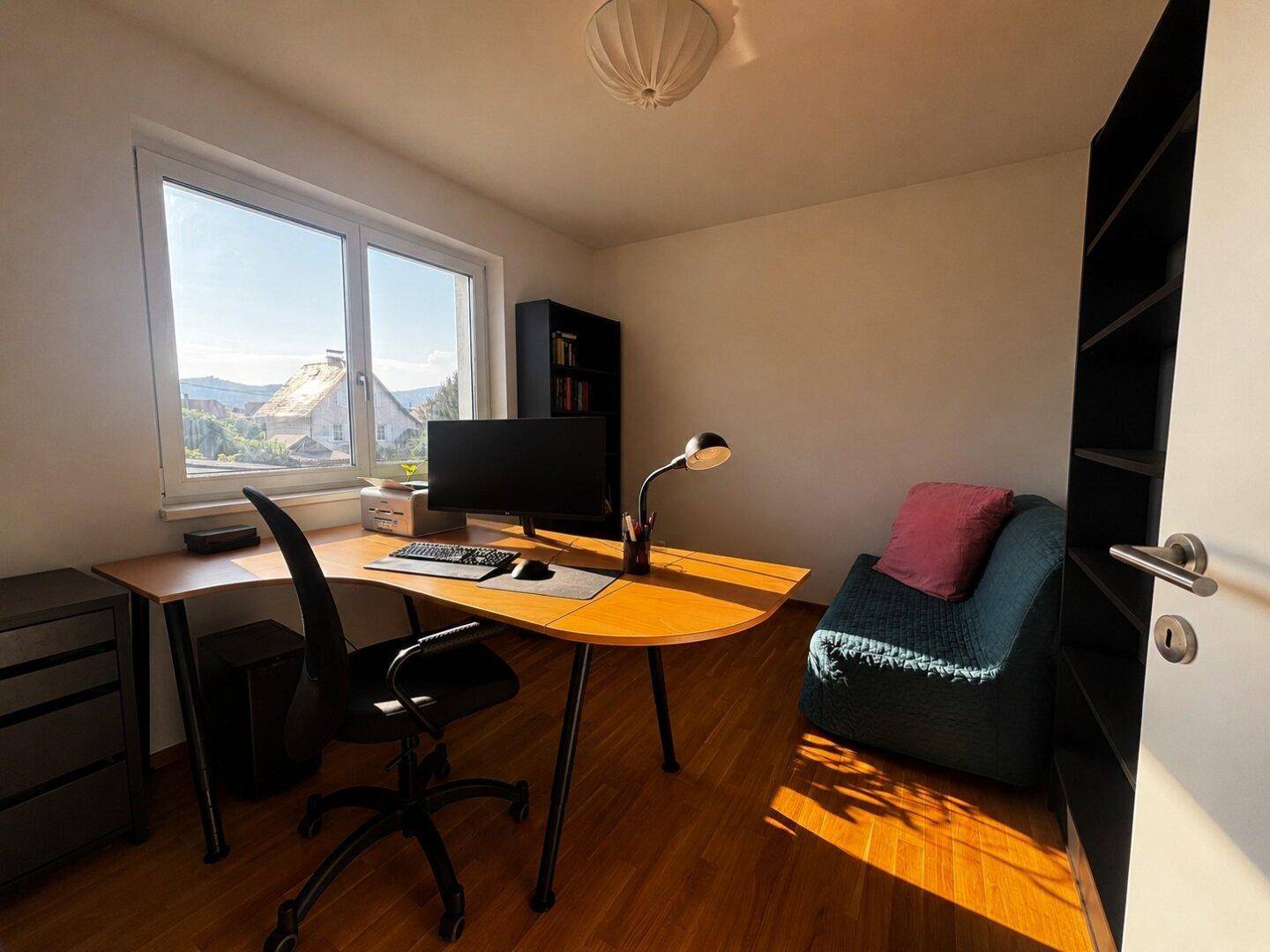 Helles Arbeitszimmer mit Schreibtisch, Bürostuhl und Blick ins Grüne.
