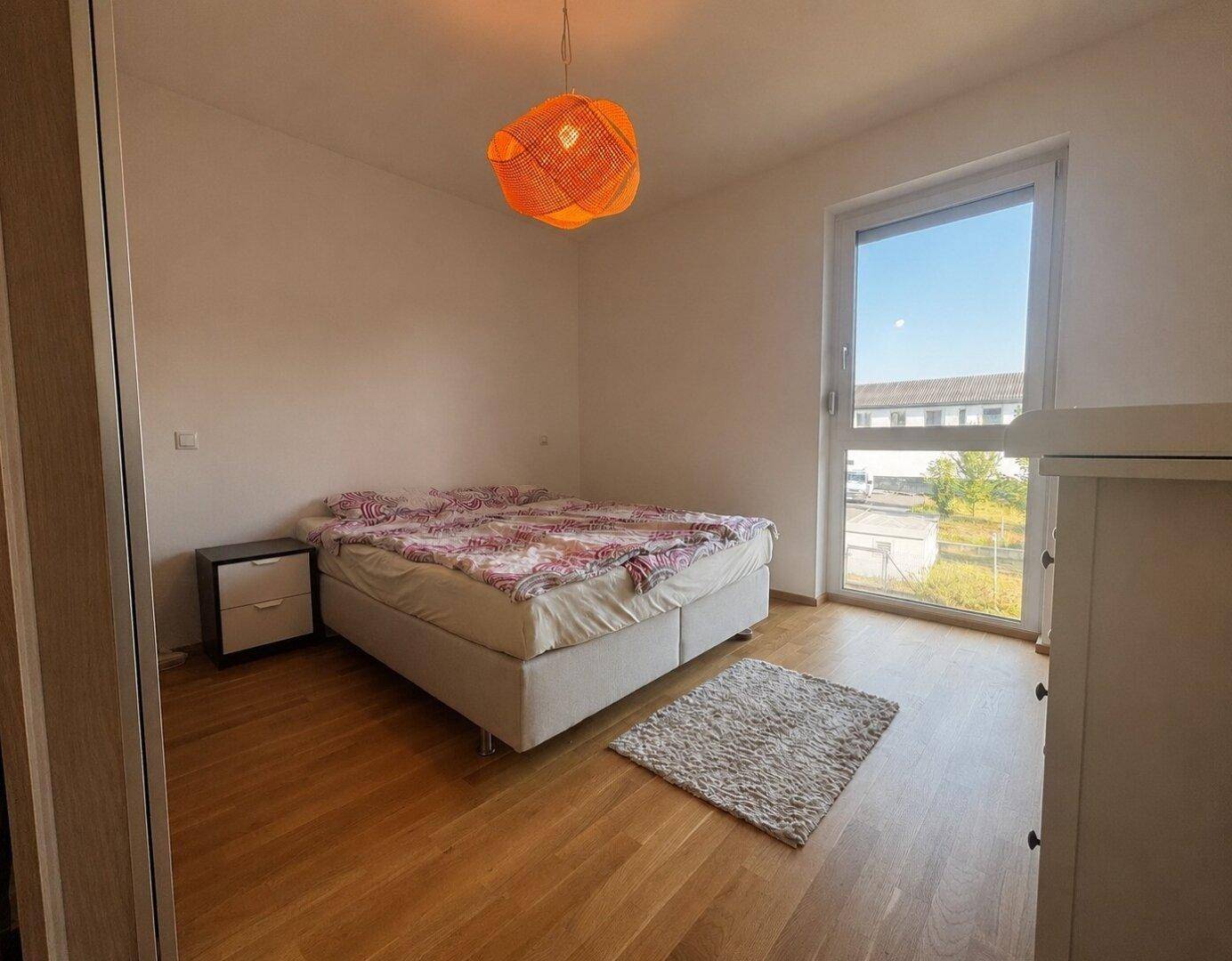 Helles Schlafzimmer mit Doppelbett, Holzboden und großem Fenster.