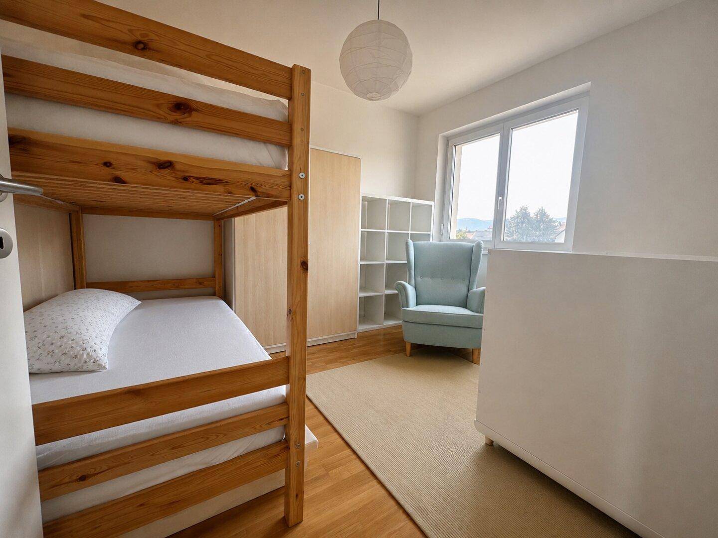 Kinderzimmer mit Etagenbett, Holzboden und viel Tageslicht durch das große Fenster.