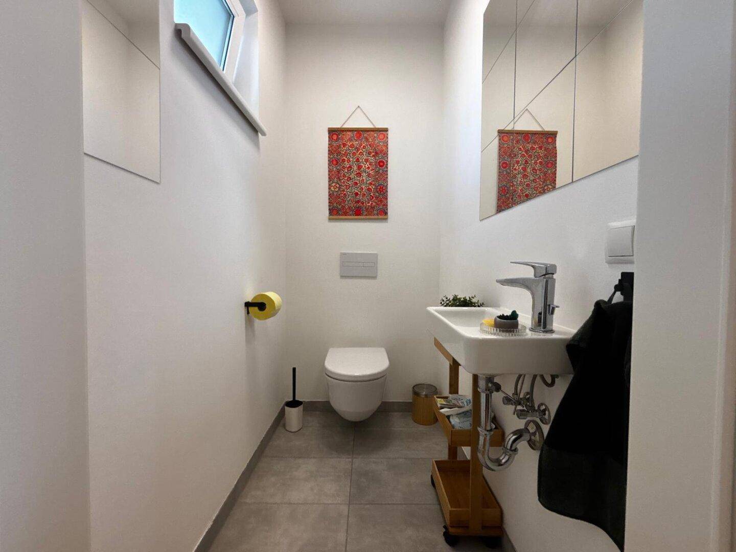 Kleines Gäste-WC mit modernem Waschbecken, Toilette und Fenster.