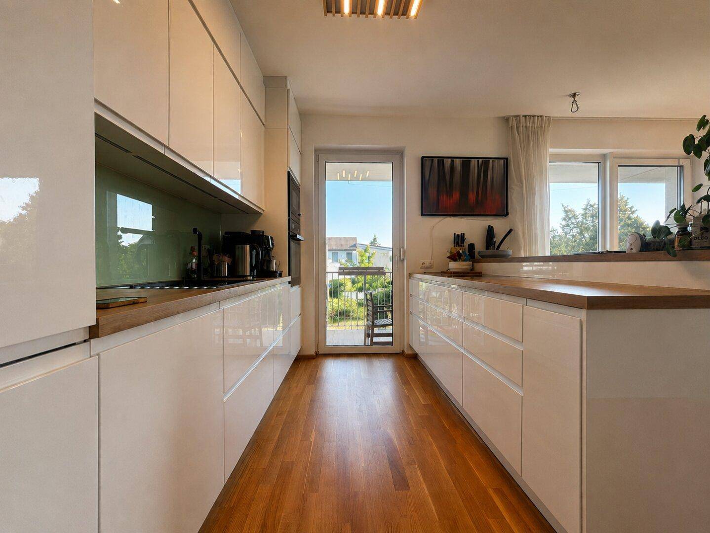 Moderne weiße Küche mit Holz-Arbeitsplatten, integrierten Geräten und Balkonzugang.