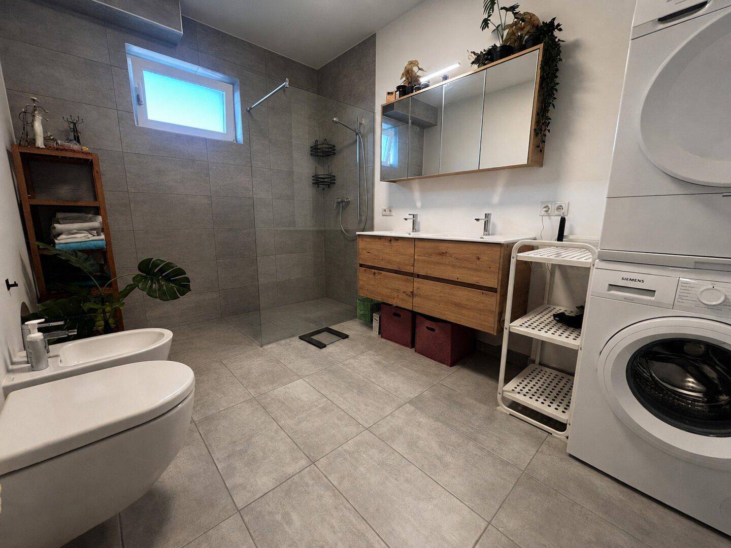 Modernes Badezimmer mit begehbarer Dusche, Doppelwaschbecken und Waschmaschine.