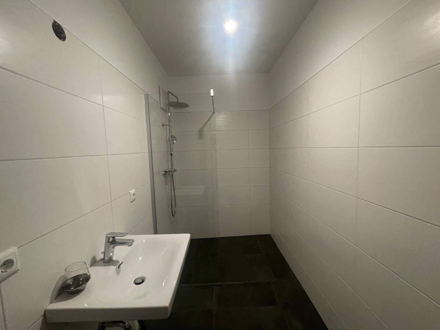 Schlichtes Badezimmer mit Dusche, Waschbecken und dunklem Fliesenboden.