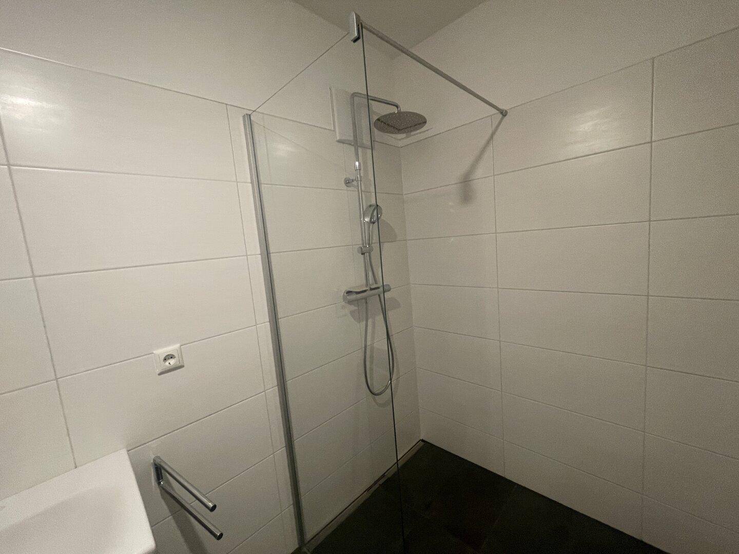 Modernes Badezimmer mit weißen Fliesen, ebenerdiger Dusche und Regenbrause.