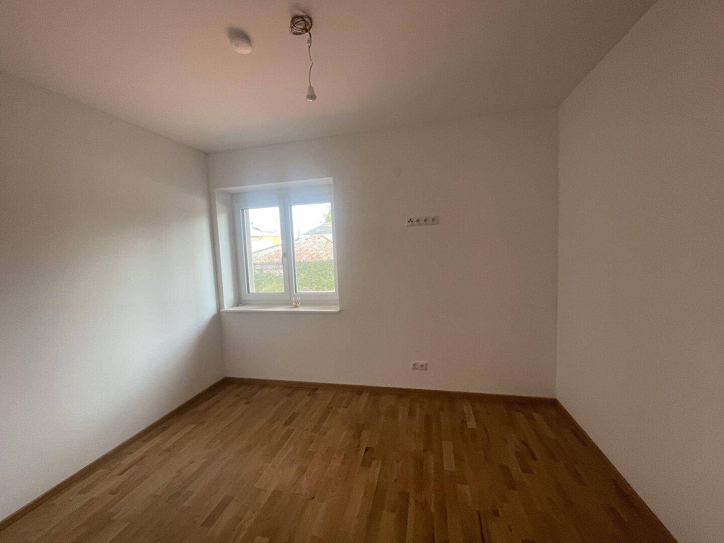 Helles Schlafzimmer mit Holzparkettboden und einem Fenster mit Blick ins Grüne.
