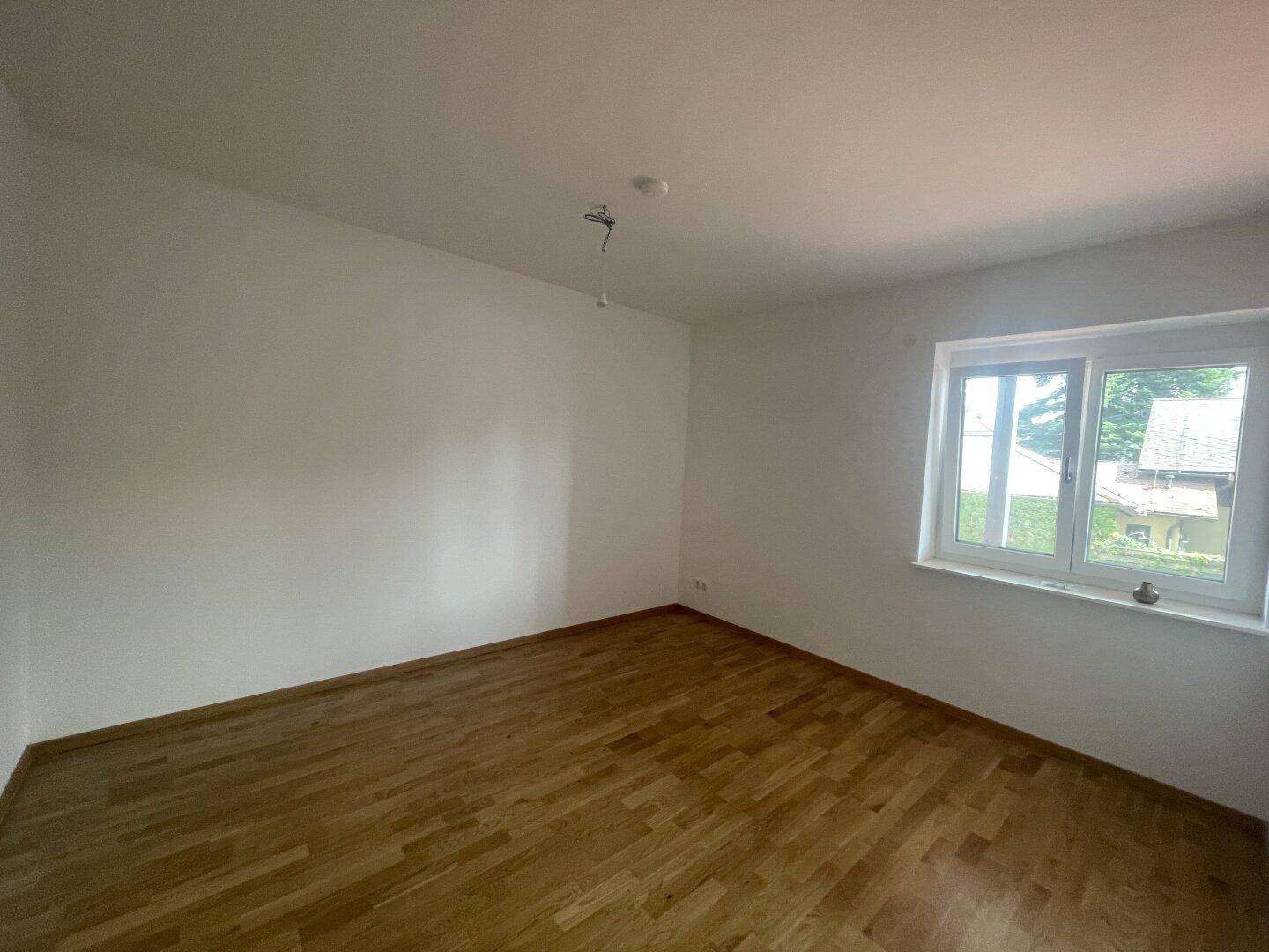 Geräumiges Schlafzimmer mit Holzparkettboden und großem Fenster für viel Tageslicht.