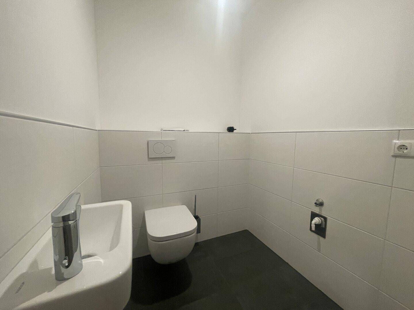 Modernes Gäste-WC mit Wand-WC, kleinem Waschbecken und dunklem Fliesenboden.