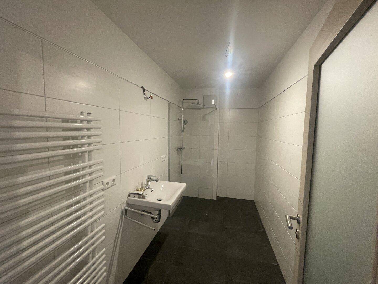 Modernes Badezimmer mit ebenerdiger Dusche, Waschbecken und beheiztem Handtuchhalter.