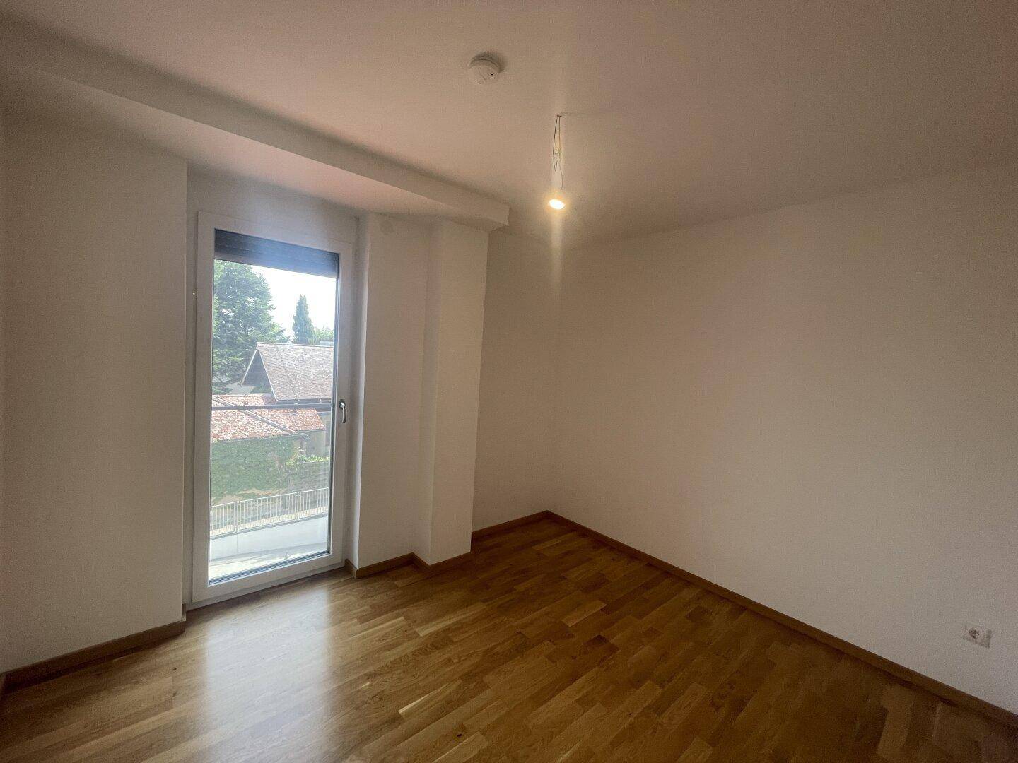 Helles Zimmer mit Holzfußboden und Zugang zu einem Außenbereich, ideal als Schlafzimmer.