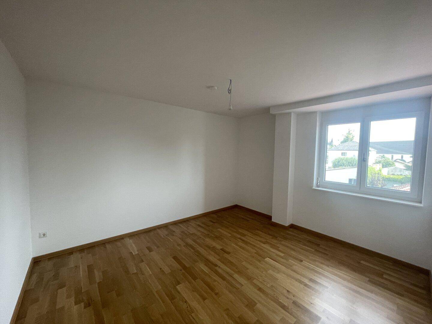 Geräumiges Zimmer mit hellem Holzfußboden und großem Fenster, das für eine angenehme Atmosphäre sorgt.