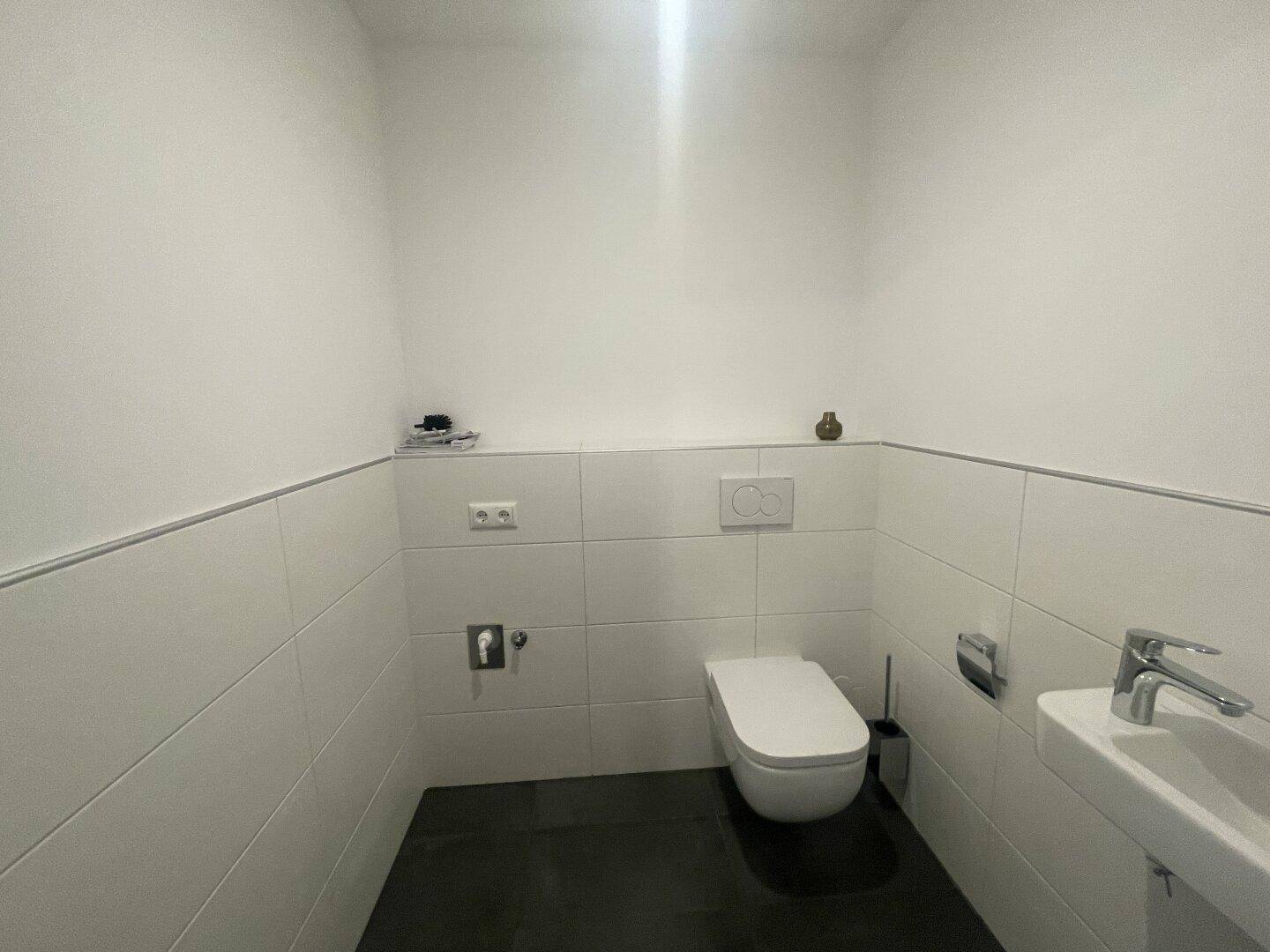 Modernes Gäste-WC mit wandhängender Toilette und kleinem Waschbecken, in schlichtem Design.