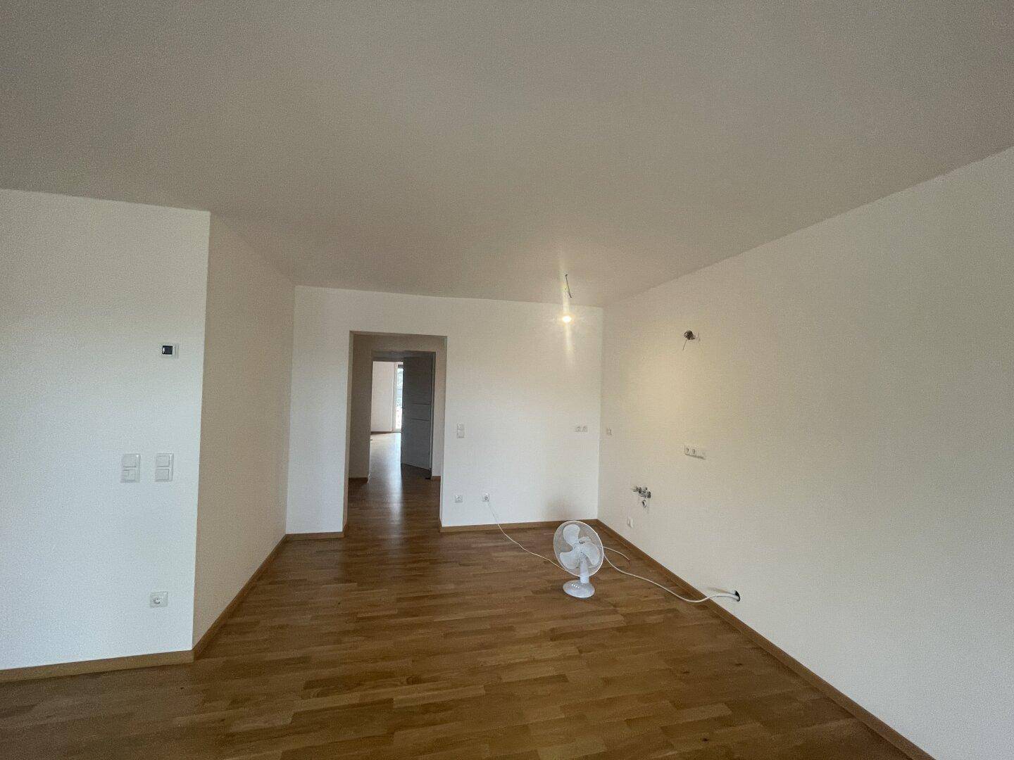 Heller Wohnbereich mit Holzfußboden und Zugang zu weiteren Räumen, bereit zur individuellen Gestaltung.