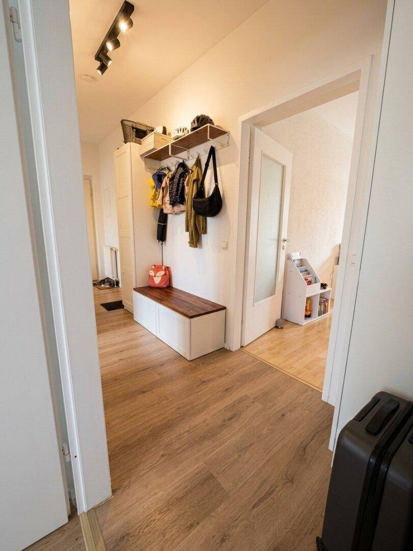 Heller Flur mit Garderobe, Sitzbank und Holzfußboden, der zu weiteren Räumen führt.