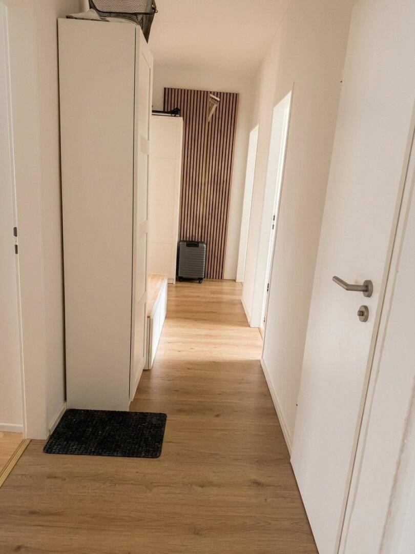 Langer, heller Flur mit Holzfußboden und einer modernen Holzvertäfelung an der Wand.