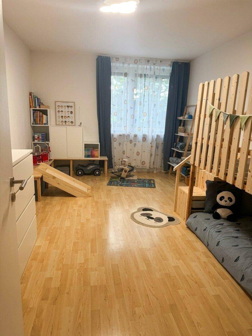 Geräumiges Kinderzimmer mit Spielgeräten, Hochbett und hellem Holzfußboden.
