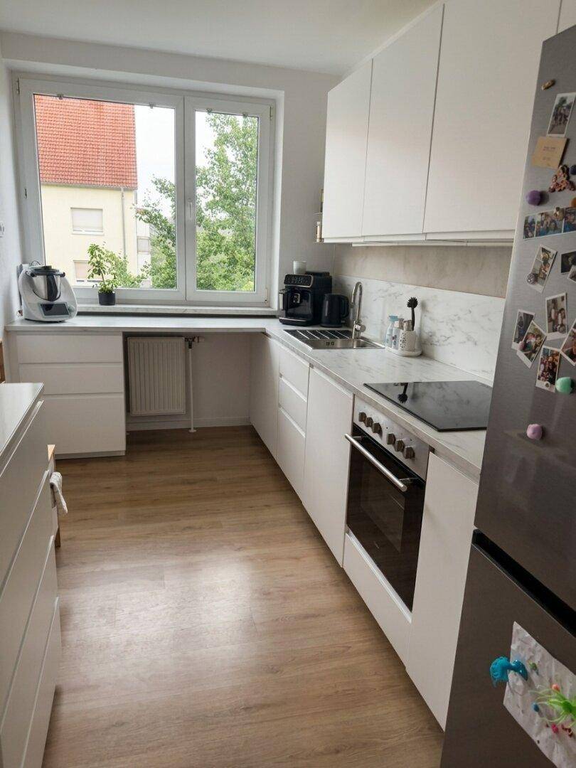 Funktionale Küche mit weißen Schränken, Holzfußboden und Blick ins Grüne durch das Fenster.