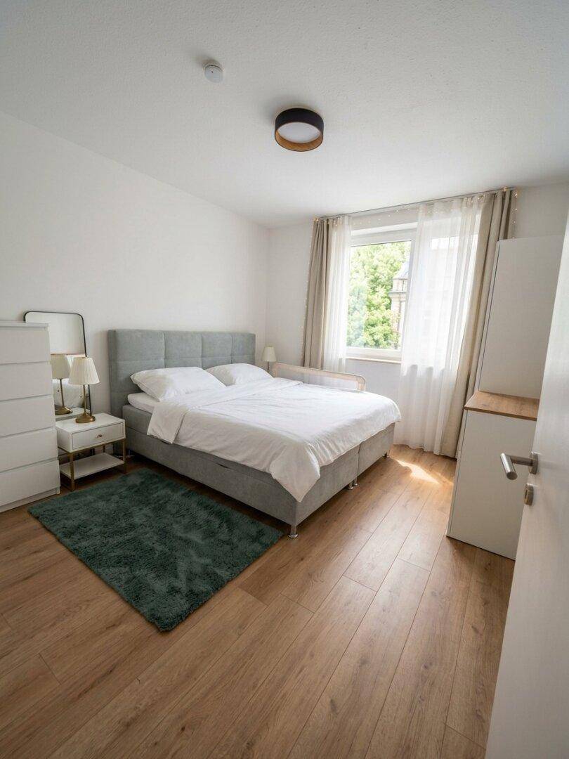 Helles Schlafzimmer mit Doppelbett, Holzfußboden und großem Fenster mit viel Tageslicht.