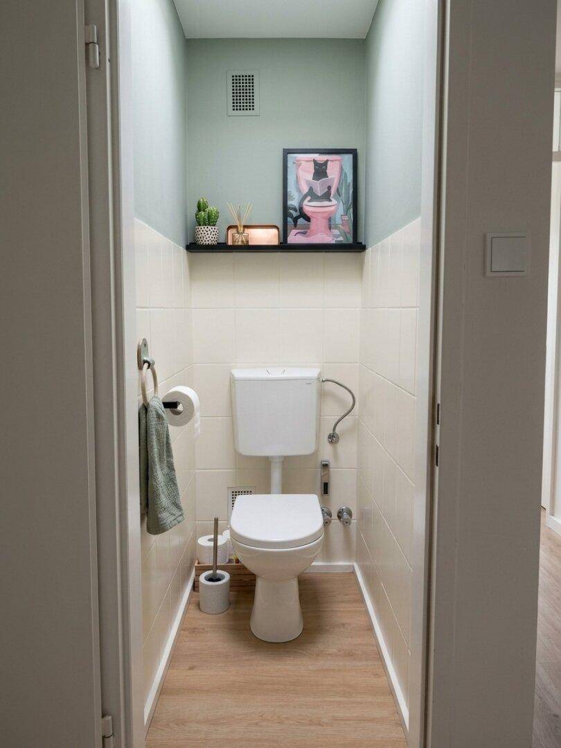 Kleines Gäste-WC mit Toilette, Holzfußboden und einer Ablage mit Dekoration.