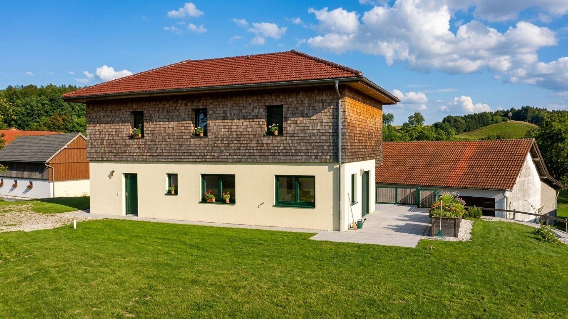 Charmantes Landhaus mit rotem Ziegeldach und Holzschindelfassade, umgeben von Grünflächen.