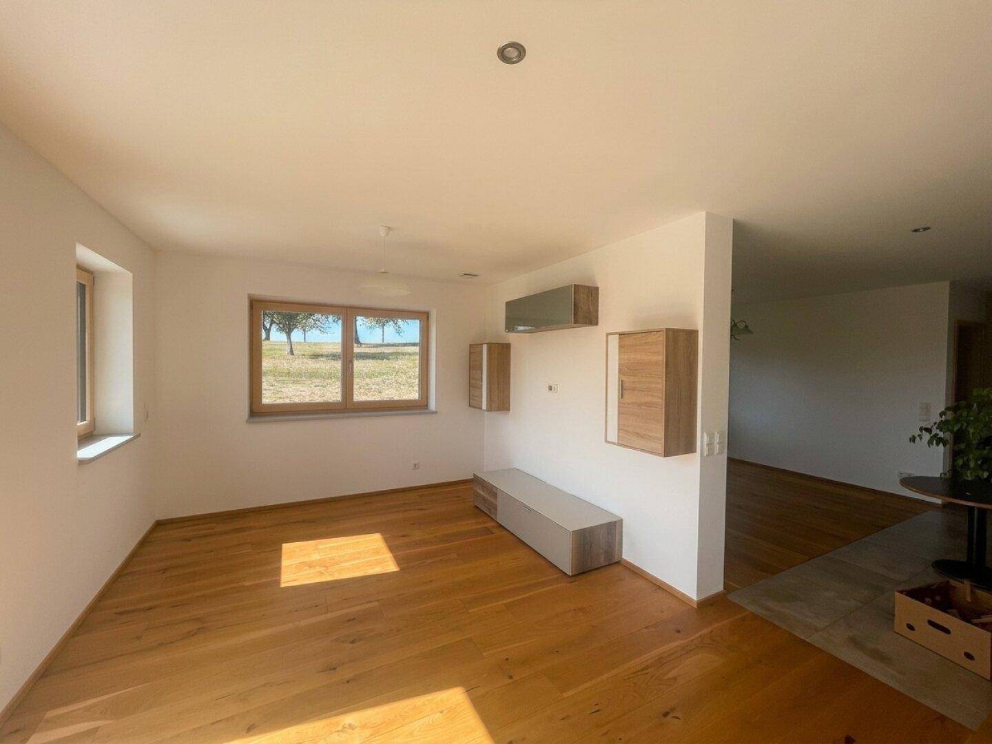 Helles Wohnzimmer mit Holzboden, großen Fenstern und Blick auf die grüne Landschaft.