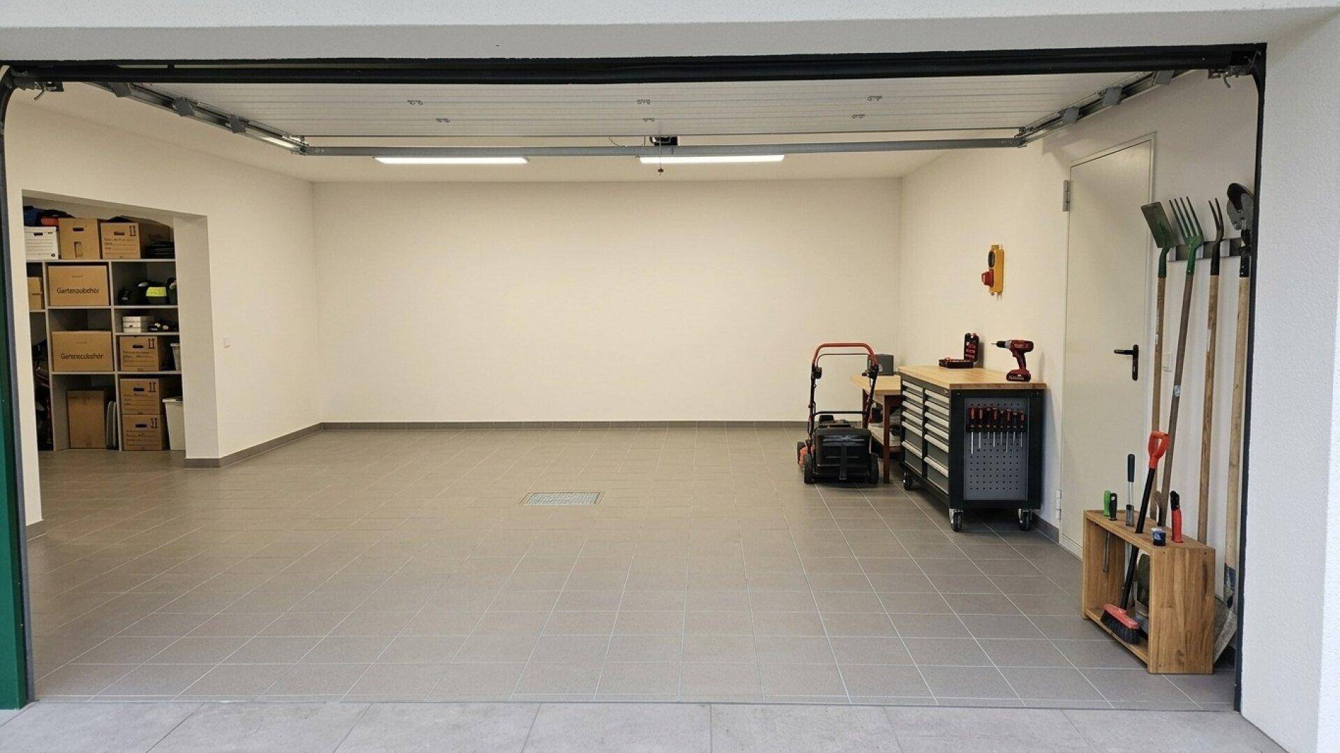 Geräumige Garage mit Fliesenboden, viel Stauraum und Platz für Fahrzeuge und Werkzeuge.
