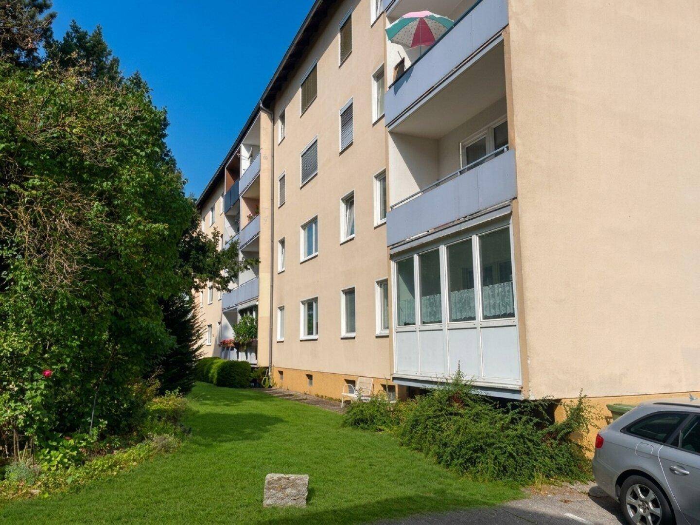 Seitenansicht des Mehrfamilienhauses mit Balkonen, teilweise verglasten Loggien und angrenzender Grünfläche.