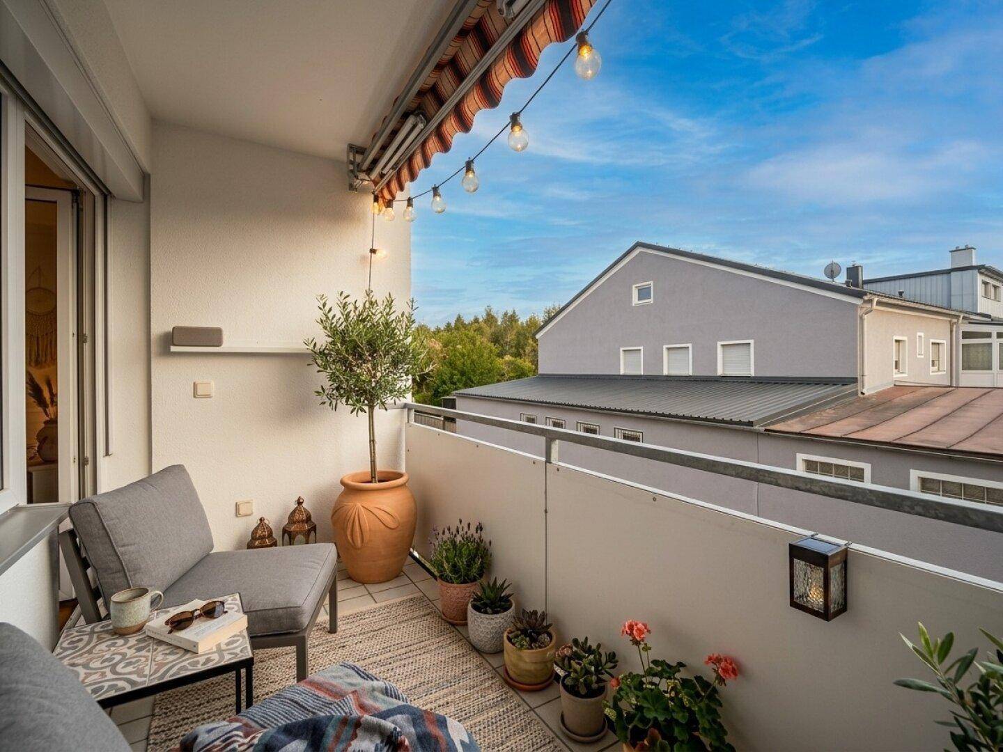 Gemütlicher Balkon mit Sitzgelegenheiten, Pflanzen und Lichterkette unter blauem Himmel.