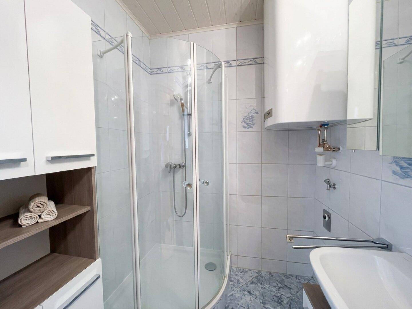 Helles Badezimmer mit Duschkabine, Waschbecken und weiß-blauen Fliesen.