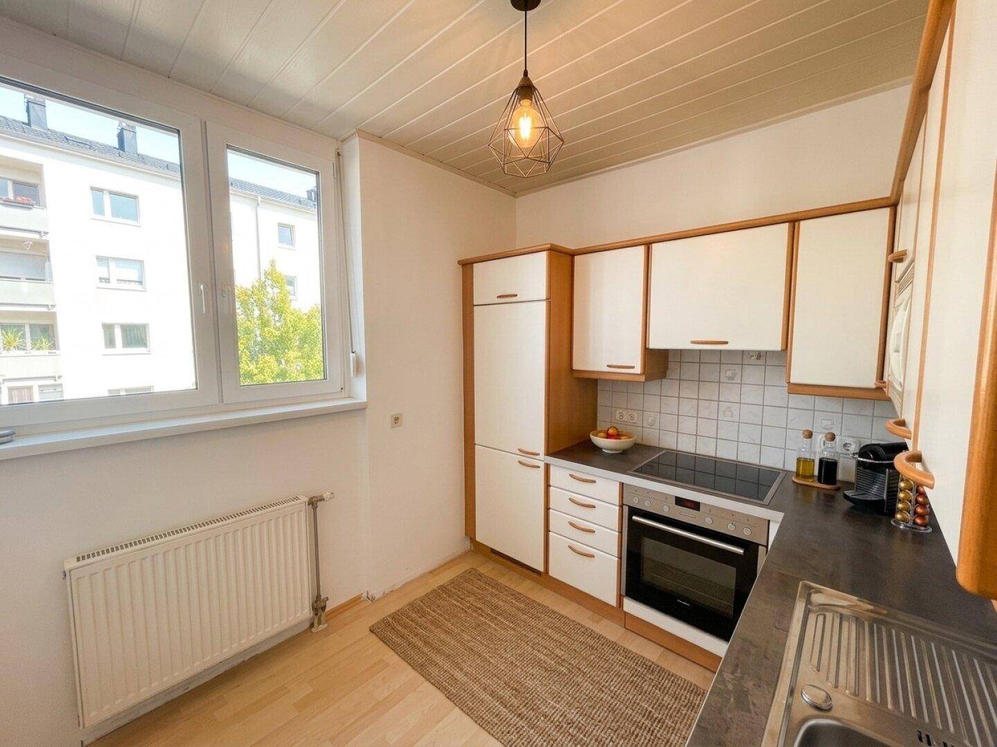 Funktionale Küche mit weißen Schränken, Holzdetails und Fenster mit Blick ins Grüne.