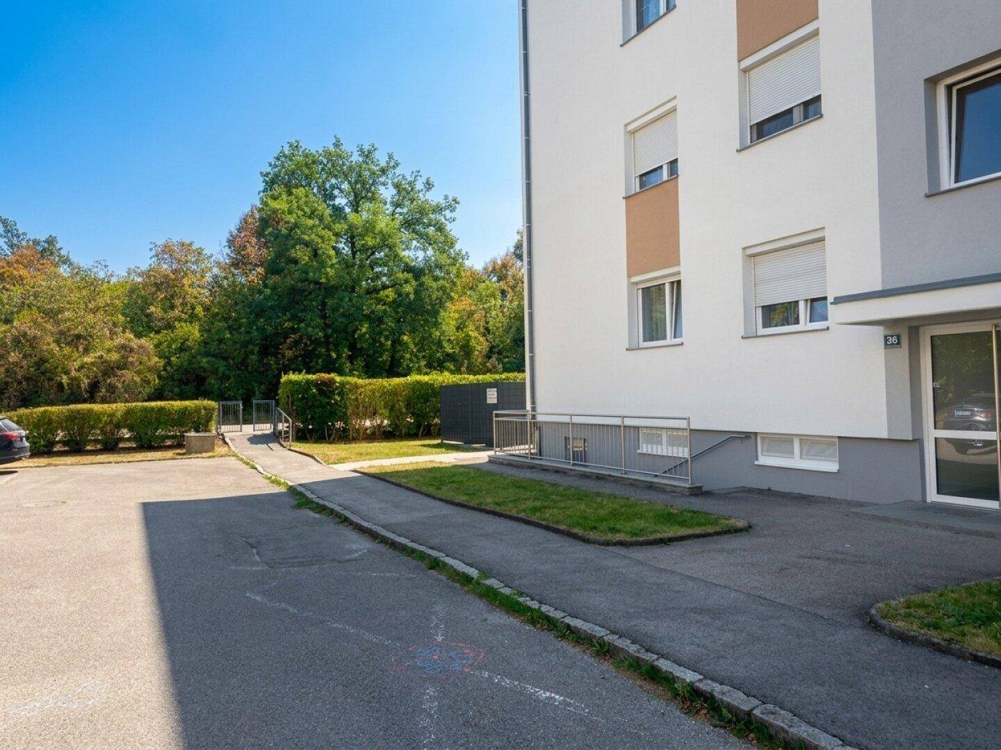 Eingangsbereich eines Mehrfamilienhauses mit Rampe und Grünfläche.
