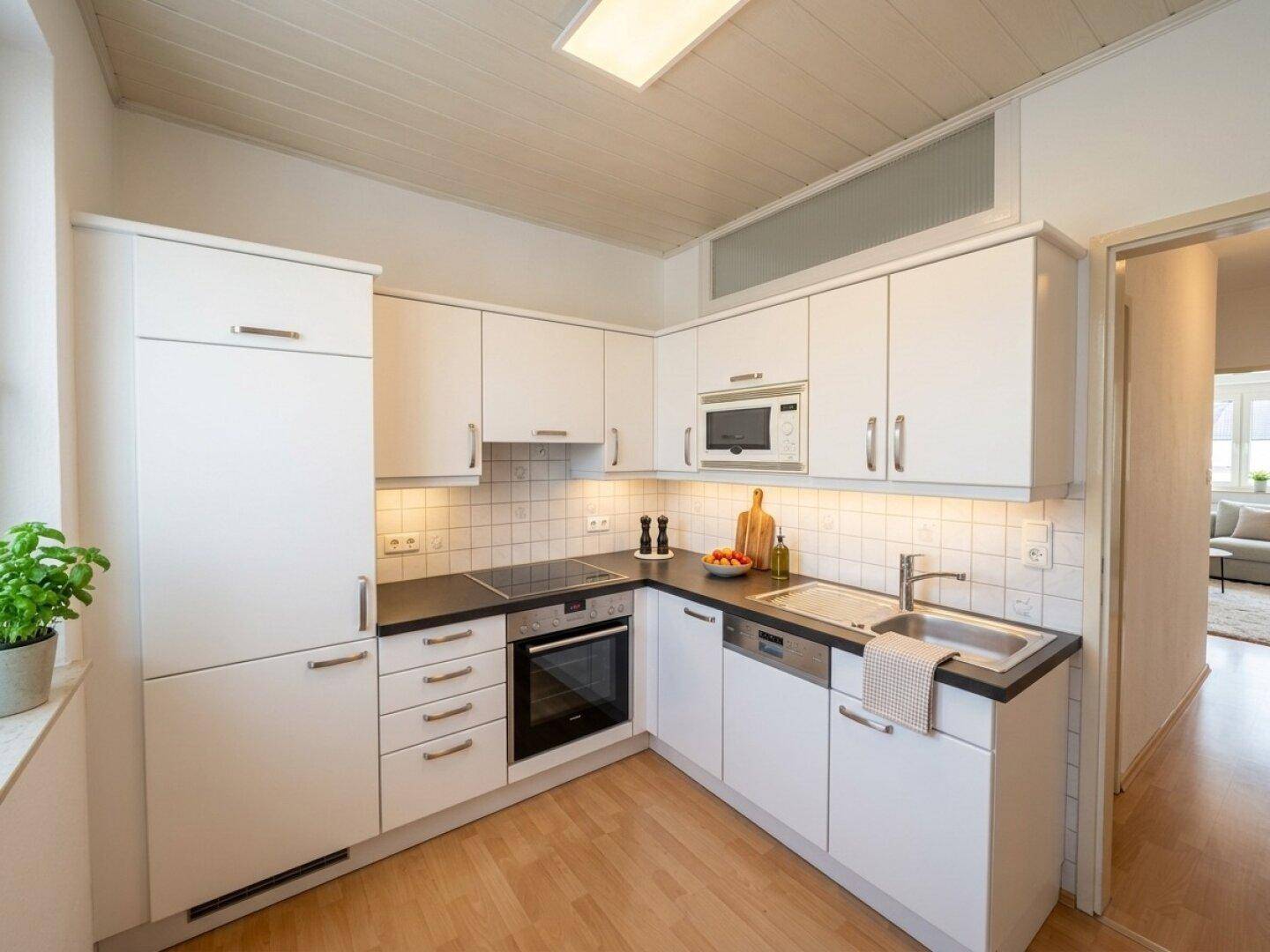 Helle Einbauküche mit weißen Schränken, dunkler Arbeitsplatte und Holzboden.