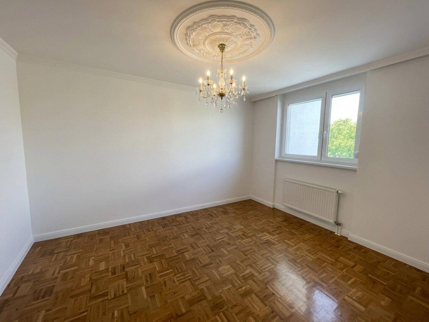 Helles Zimmer mit Parkettboden, Kronleuchter und Stuckdecke.