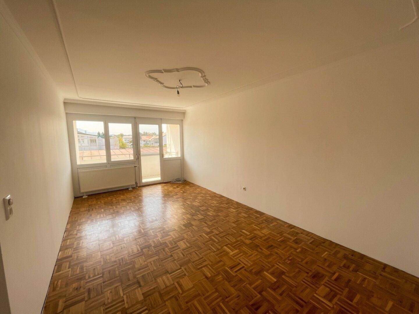 Geräumiges Zimmer mit Parkettboden und Zugang zum Balkon.