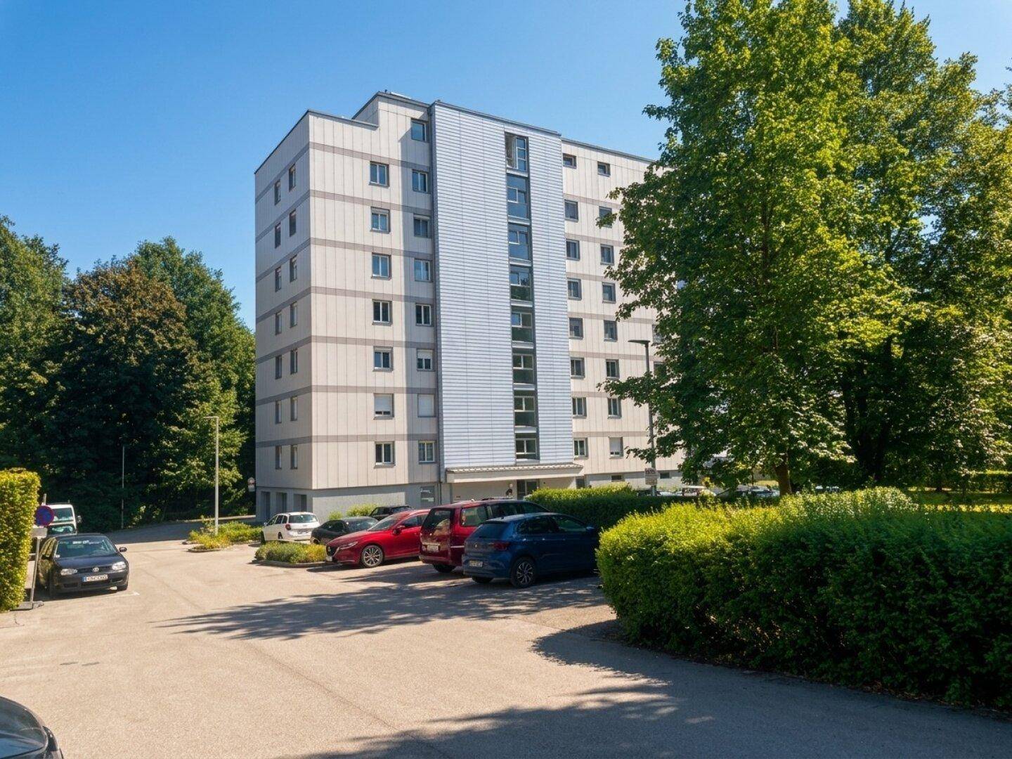 Modernes Mehrfamilienhaus mit mehreren Stockwerken und Parkplätzen im Freien an einem sonnigen Tag.