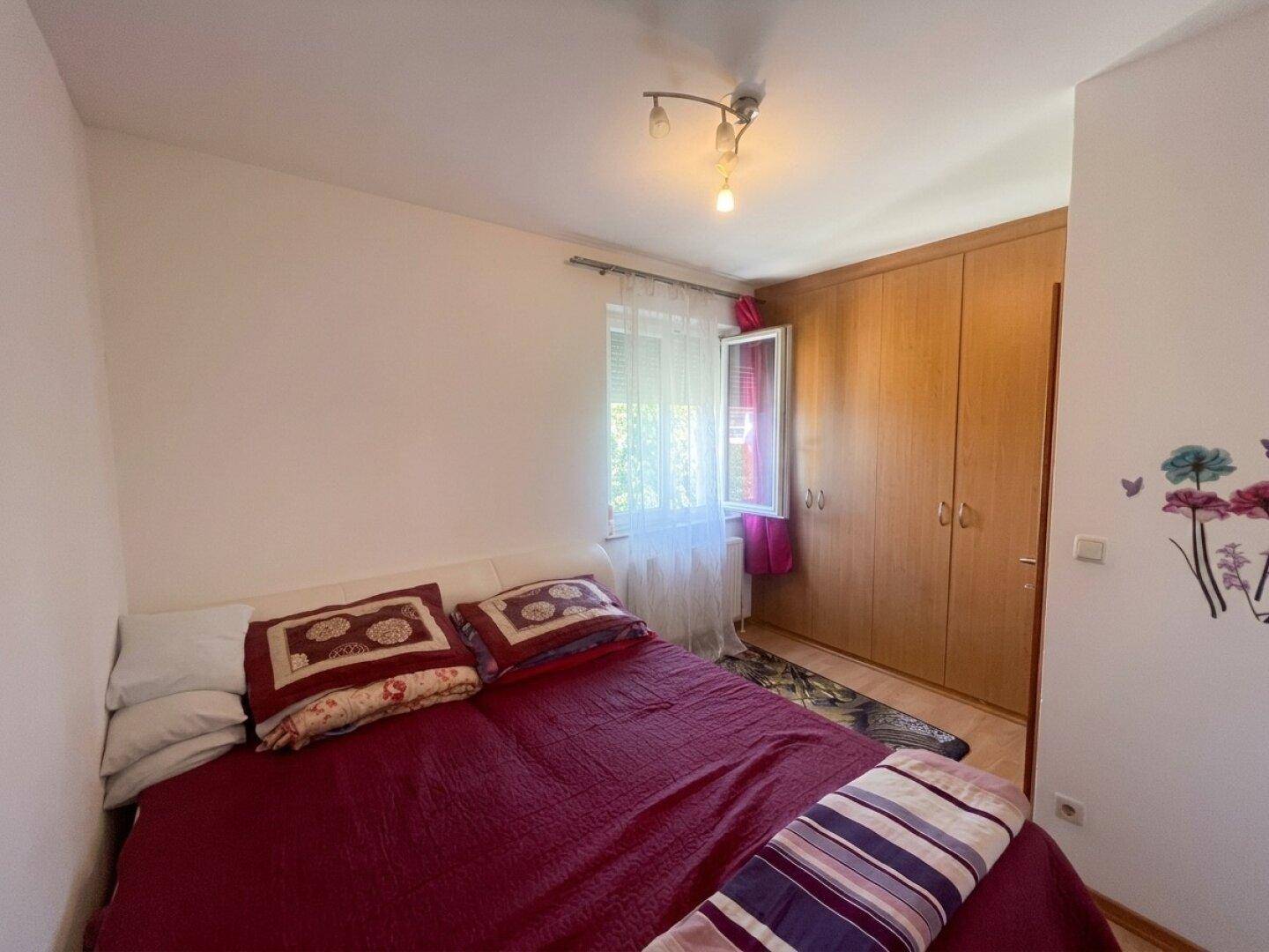 Gemütliches Schlafzimmer mit Doppelbett, großem Holzschrank und Fenster mit Blick ins Grüne.