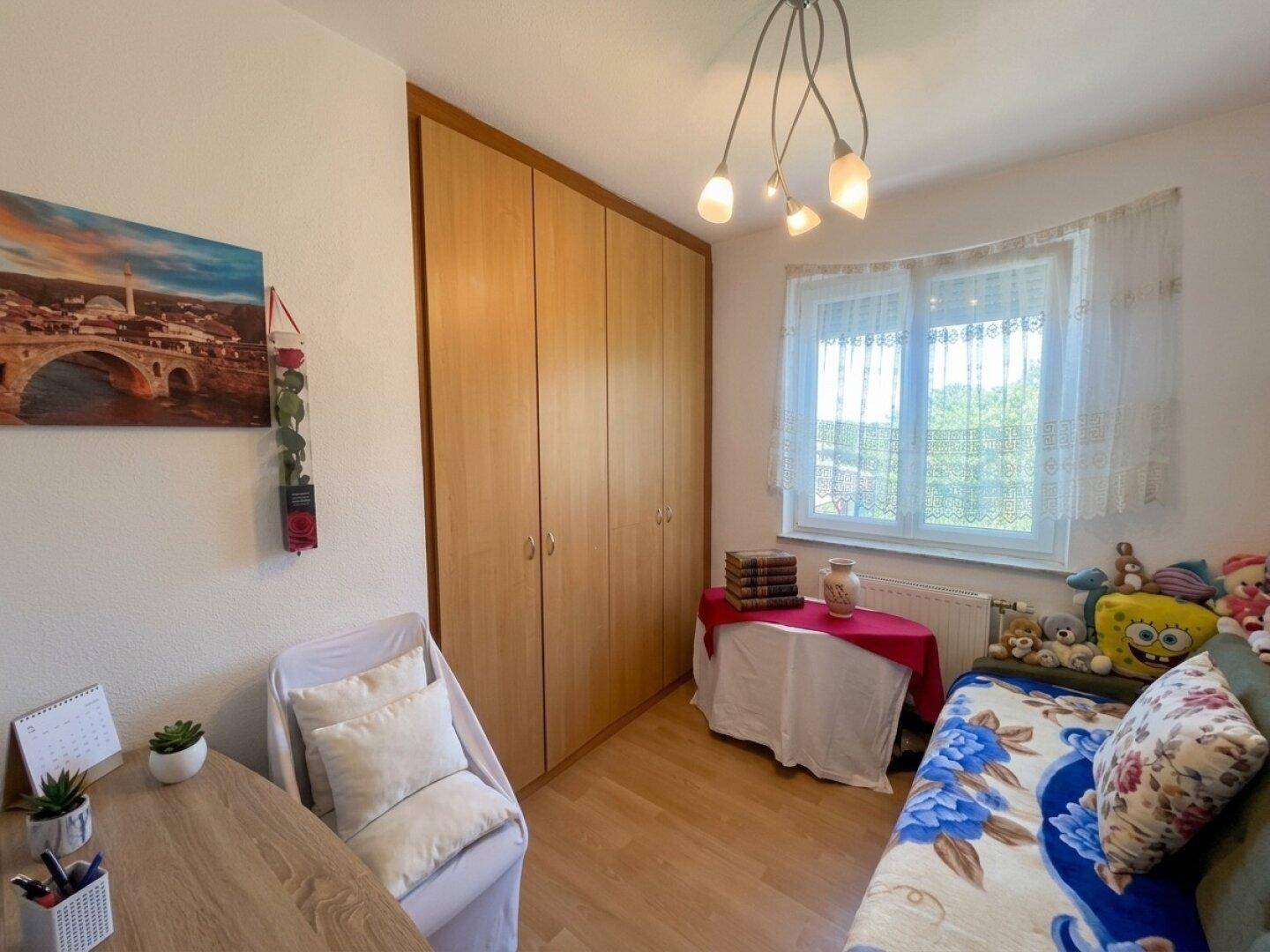 Helles Kinder- oder Gästezimmer mit Holzschrank, Schreibtisch und Fenster, freundlich eingerichtet.